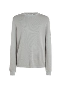 Camisa de jersey de manga larga de color gris claro con un patrón texturizado, cuello redondo y mangas con puños. Presenta un parche de logo en la manga izquierda.