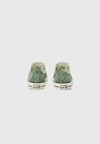 Adidași din pânză cu model de șarpe verde, având talpa din cauciuc crem, cu un design low-top și branding contrastant negru pe călcâi.