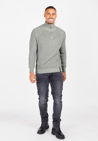 Pulover gri cu nervuri, guler înalt și fermoar pe jumătate, purtat împreună cu blugi închisi și cizme negre cu șireturi pentru un look casual.
