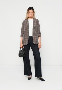 Blazer a quadri con maniche arrotolate, top bianco, jeans larghi scuri, borsa nera, scarpe con tacco a punta nere. Design pulito e strutturato.