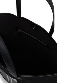 Crni platneni toter s kožnim detaljima. Unutrašnjost sadrži džep na zip, a tekstura je glatka i mekana. Dizajn bez zatvaranja na vrhu.