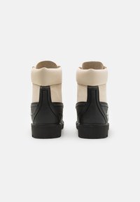 Zapatillas altas en negro y beige que presentan un material texturizado, puntera redondeada, cuello acolchado y panel del talón en contraste.