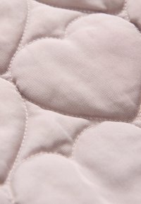 Tejido acolchado en un suave tono rosa, con un patrón de corazones que presenta surcos texturizados y secciones lisas, destacando las costuras detalladas.