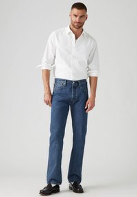 Camicia bianca con bottoni, jeans in denim blu, vestibilità dritta, scarpe in pelle marrone scuro, design semplice, senza motivi o loghi visibili.