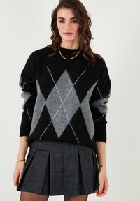 Zwart-grijze argyle-patroon trui met losse mouwen, gecombineerd met een grijze plissérok. Het model draagt een eenvoudige gouden ketting.