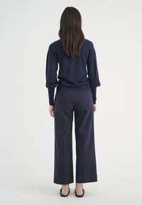 Granatowy sweter z dzianiny z bufkami na rękawach, w połączeniu z szerokimi spodniami z wysokim stanem, oba w dopasowanym, ciemnym kolorze.