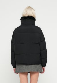 Crna jakna na naduvavanje s visokim ovratnikom, s ukrasom od umjetnog krzna. Dizajn uključuje horizontalne šavove i elastične manžete za pristajanje.