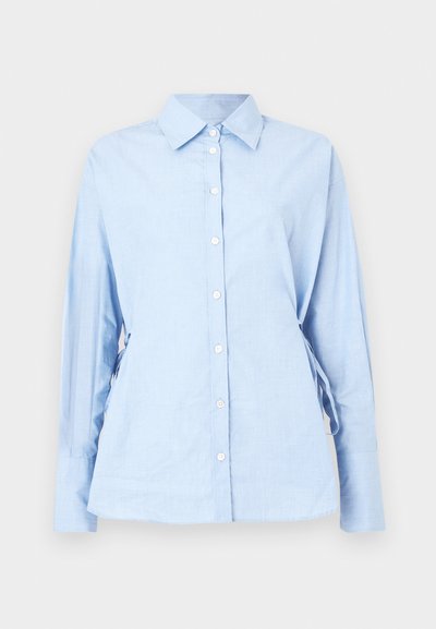 Ανοιχτό γαλάζιο πουκάμισο με μακριά μανίκια από απαλό ύφασμα. Διαθέτει κλείσιμο με κουμπιά μπροστά, γιακά και ρυθμιζόμενα κορδόνια στα πλαϊνά για εφαρμογή.