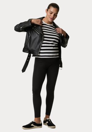 Sort læder bikerjakke over en stribet skjorte med korte ærmer, parret med sorte leggings og sorte sneakers med cremefarvede detaljer.