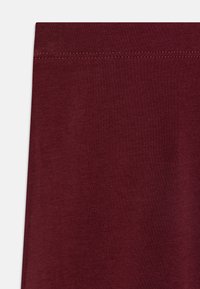 Burgundi rugalmas anyag sima textúrával, amelynek felső széle tiszta befejezésű. Nincsenek látható minták vagy fém alkatrészek.