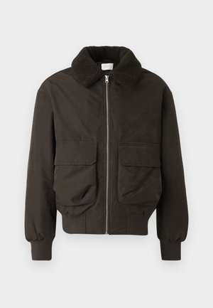 Temnozeleni plašč s teksturiranim krznom okoli ovratnika. Ima sprednje žepke in zadrgo. Narejen je iz gladkega blaga z rebrastimi manšetami.