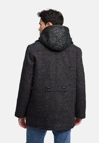 Abrigo con capucha en tejido de tweed oscuro con un patrón de espiga y capucha de punto en contraste. Presenta dos botones en la parte posterior y mangas de corte recto.