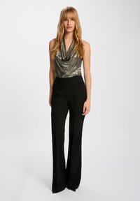 Body con color plata metálico con cuello drapeado, combinado con pantalones negros de cintura alta y acampanados, que presentan un ajuste elegante y un diseño minimalista.