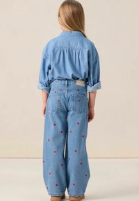 Chemise en denim à coupe décontractée, accompagnée d'un jean bleu clair avec des broderies de cœurs rouges et une coupe large, vue de dos.