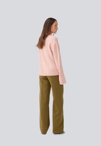Pull léger rose avec une coupe décontractée et un ourlet côtelé, associé à un pantalon large vert olive. Vue arrière à plat, textures lisses.