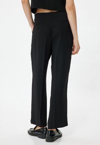 Svarta vida byxor med en slät textur, som har två bakfickor och en skräddarsydd passform. Kommer med glänsande svarta skor.