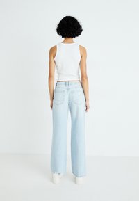 Αντίκες ανοιχτού μ�πλε τζιν με πλατιά γραμμή και ψηλή μέση, πεντάτσεπτο σχέδιο και ελαφριά φθορά, συνδυασμένα με κοντομάνικη λευκή μπλούζα.