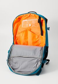 Turkis og svart ryggsekk med oransje interiør, som har en stor hovedkompartement, grå polstret del og flere lommer.