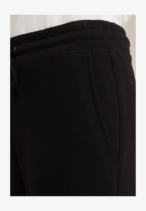 Musta collegehousut, jotka on valmistettu pehmeästä puuvillasekoitekankaasta. Varustettu naruompeluvyöllä, sivutaskuilla ja sileällä pinnalla.