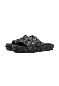 Sandali in pelle nera con design superiore intrecciato, punte aperte e suola testurizzata. Accentuati da dettagli intrecciati lungo i bordi.