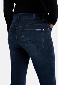 Mörkblå denimjeans med en figurnära design. Funktioner inkluderar två bakfickor och en liten märkesskylt på höger ficka. Strukturerad tyg.
