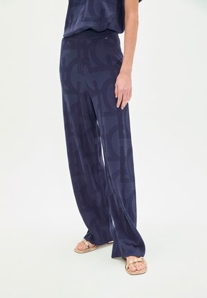 Pantalones anchos azul marino con un patrón geométrico texturizado, tela suave y una cintura cómoda, combinados con sandalias planas.