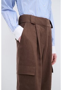 Braune Leinenhose mit hoher Taille, seitlichen Taschen und lockerer Passform, kombiniert mit einem blau-weißen gestreiften Hemd.