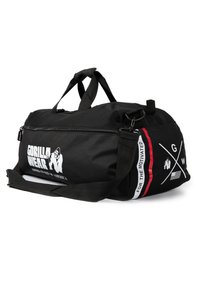 Black gym duffel bag made of durable fabric, featuring a zip closure, double handles, and a removable shoulder strap with logo and accents.