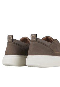 Sneakers in suede marrone con suola in gomma bianca, forma rotonda e linguette sul tallone marchiate con testo dorato. Texture liscia e design minimal.