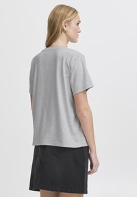 Pilkas trumpas rankovėmis marškinėliai, su laisvu siluetu, pagaminti iš minkštos medžiagos, derinami su juoda džinsine sijonku, turinčiu galinį kišenės dizainą.