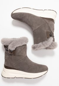 Stivali in suede grigi per l'inverno con suole spesse bianche, rivestimento in pelliccia morbida sulla parte superiore e chiusure a toggles sui lati.