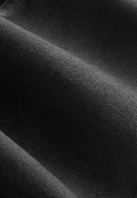 Texturovaná černá tkanina s měkkým matným povrchem, která ukazuje jemné detaily tkaní a mírné záhyby, odrážející světlo v různých intenzitách.