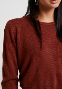 Bordeauxkleurige gebreide sweater met een structuurpatroon, ronde hals en lange mouwen. Heeft delicate stiksels en een zachte, warme uitstraling.