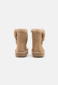 Bottines en suède tan avec une doublure en fourrure douce et un revers, forme arrondie, semelle plate et détails de couture visibles.