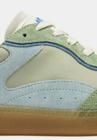 Zapatilla de color verde claro y azul con materiales de ante y tela, con una suela texturizada y detalles cosidos. Incluye ojales para cordones.