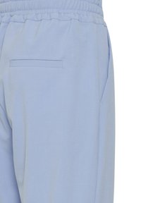 Svetlo modri hlače z gladko teksturo, ki imajo elastični pas in diskreten zadnji žep za dodatno funkcionalnost.