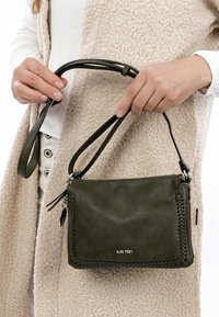Borsa a tracolla in pelle verde con dettagli intrecciati, una tracolla removibile e chiusura a cerniera. Esibita su un indumento beige testurizzato.