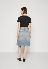 Svart t-skjorte med korte ermer og lyseblå denim A-linje skjørt med rå kant, som har baklommer og høy midje design. Svart sko.