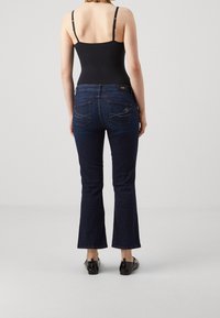 Vaqueros acampanados de un azul oscuro con una altura media, tejido de mezclilla texturizado, costuras en contraste y bolsillos decorativos. Top sin mangas negro.
