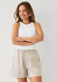 Lichtbeige linnen shorts met zijzakken en een elastische trekkoord taille, gecombineerd met een witte ribbel tanktop. Eenvoudig, casual ontwerp.