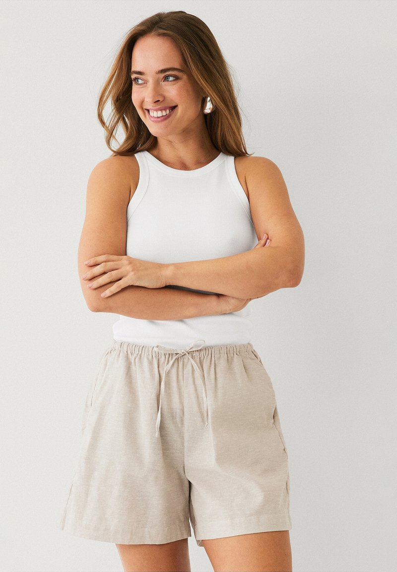 Lichtbeige linnen shorts met zijzakken en een elastische trekkoord taille, gecombineerd met een witte ribbel tanktop. Eenvoudig, casual ontwerp.