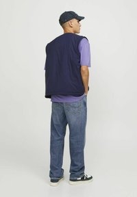 Gilet marine sur un t-shirt violet, associé à un jean bleu clair et des baskets noires. Le gilet présente un tissu texturé et une coupe décontractée.