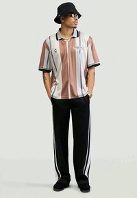 Polo de mangas curtas com riscas em cores pastel e um colarinho preto, combinado com calças pretas com riscas brancas laterais e um chapéu tipo balde.