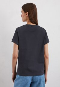T-shirt in cotone grigio con scollo rotondo e maniche corte, mostrato da dietro, abbinato a un jeans blu. Tessuto morbido.