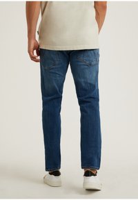 Tmavě modré džíny z denimu s rovnými nohavicemi, vybavené zadními kapsami a jemným vyblednutím, doplněné bílými teniskami.