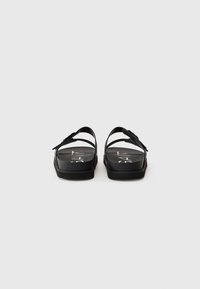 Black sandals with a flat sole, two adjustable straps, and a smooth matte finish. Features a bold logo on the footbed.