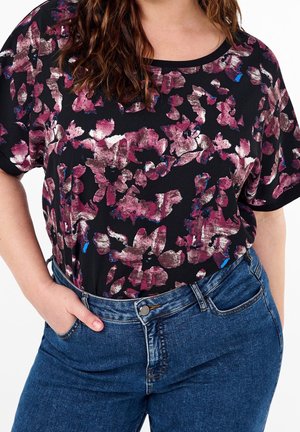 Maglietta nera con motivo floreale viola e bianco, maniche corte e scollatura rotonda, abbinata a jeans di denim blu scuro.