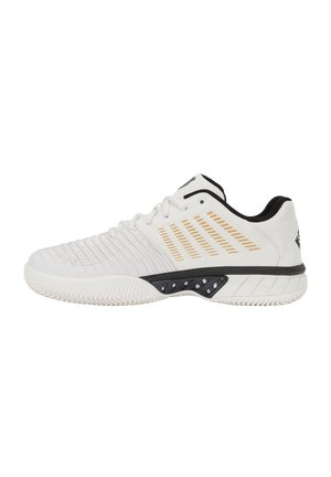 Chaussure de sport blanche avec des accents noirs et dorés, semelle texturée, laçage à l’avant et col matelassé pour le soutien et le confort.