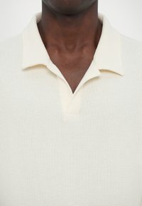 Vit polo-shirt med en texturerad väv, med krage av klassisk modell, en knappslå med två knappar och en avslappnad passform.