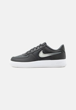 Baskets Nike basses noires avec semelle blanche et logo Swoosh argenté, présentées sur un fond gris clair uni.